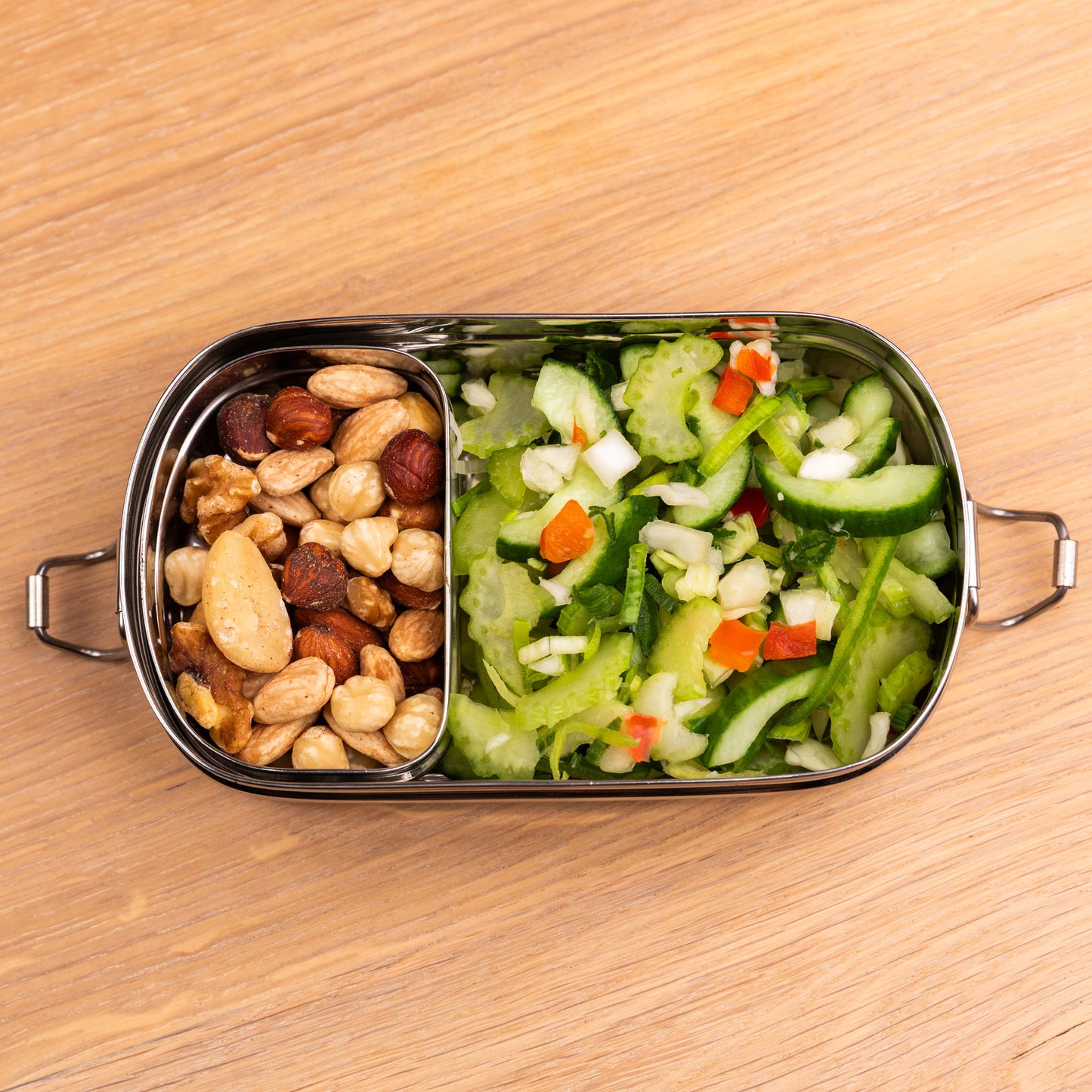 RVS bento lunchbox gevuld met noten en salade op een schooltafel