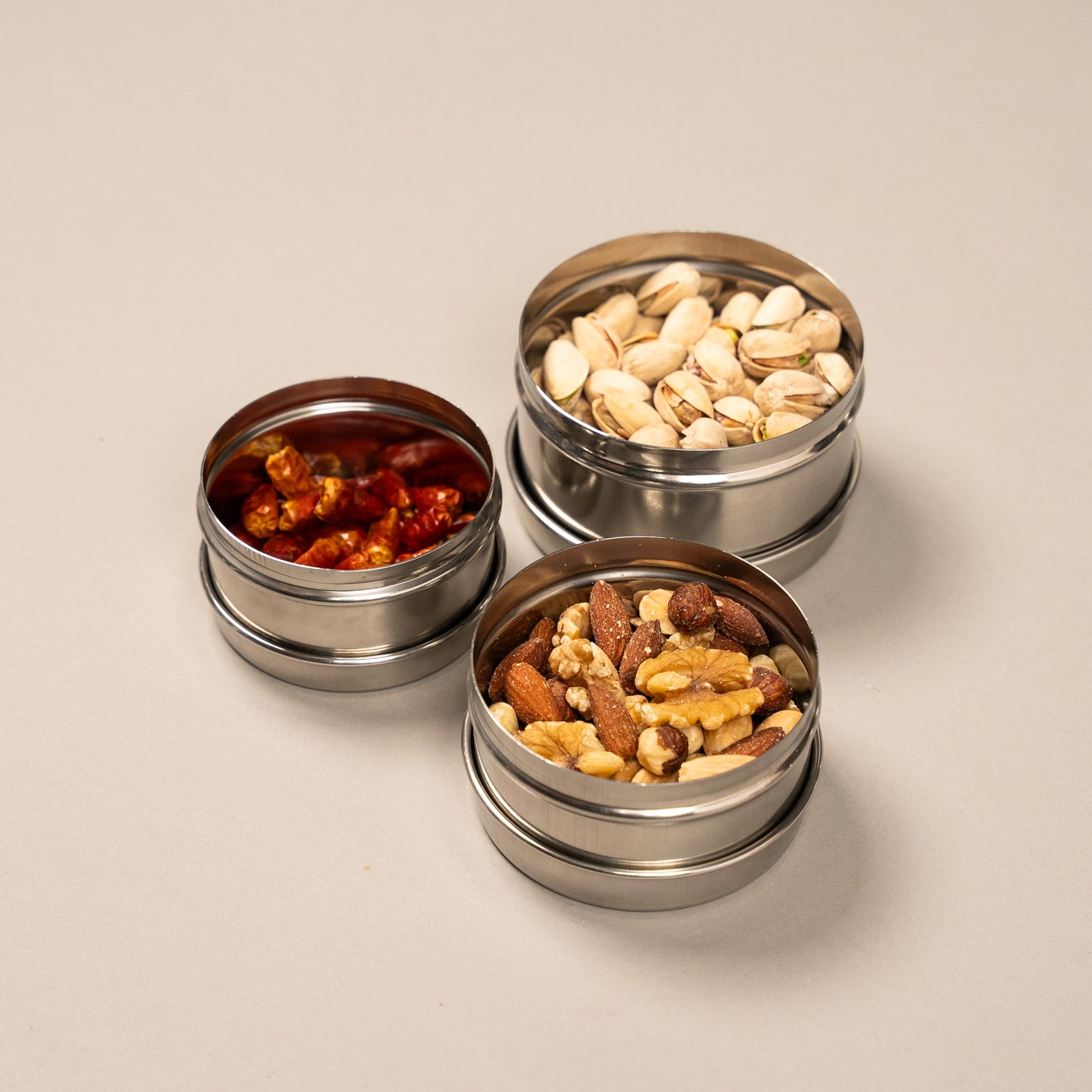 3 kleine RVS voorraadpotjes gevuld met pepers en pistachenoten
