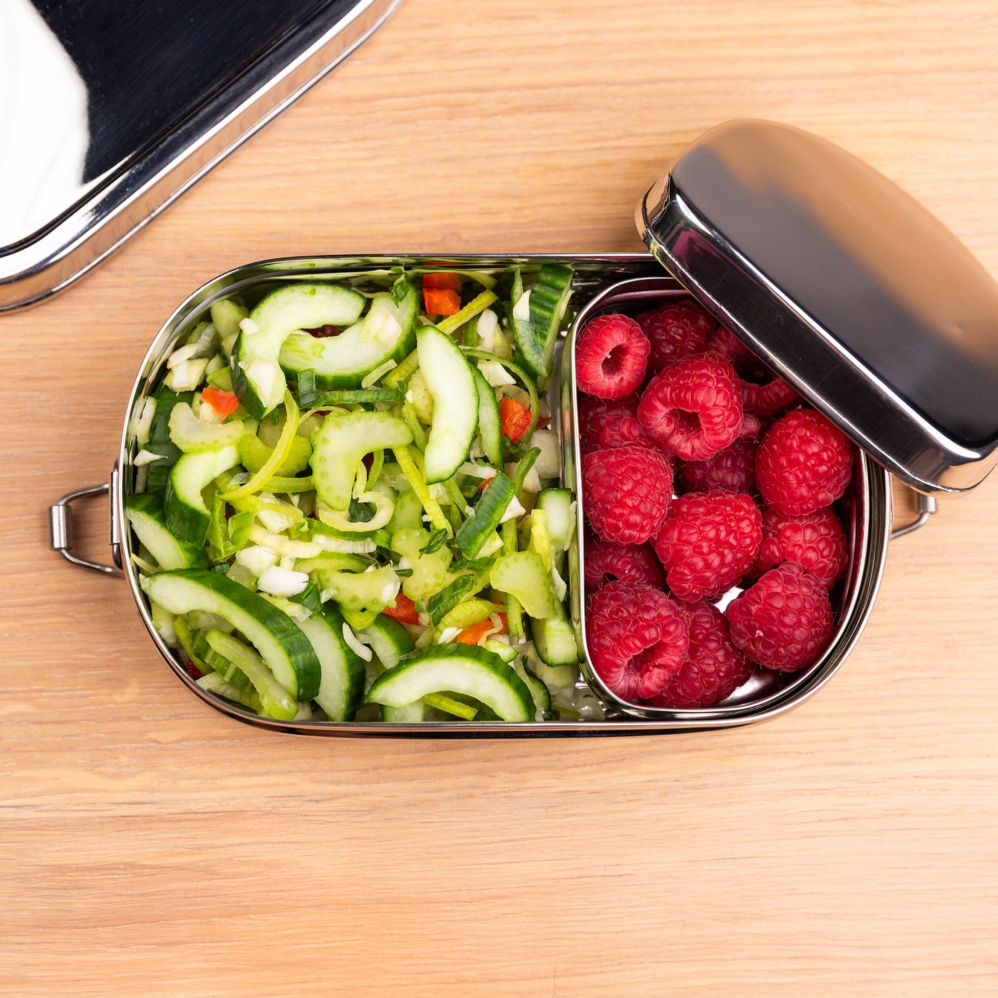 RVS lunchbox voor kinderen van boven gevuld met salade en framboos op een schooltafel