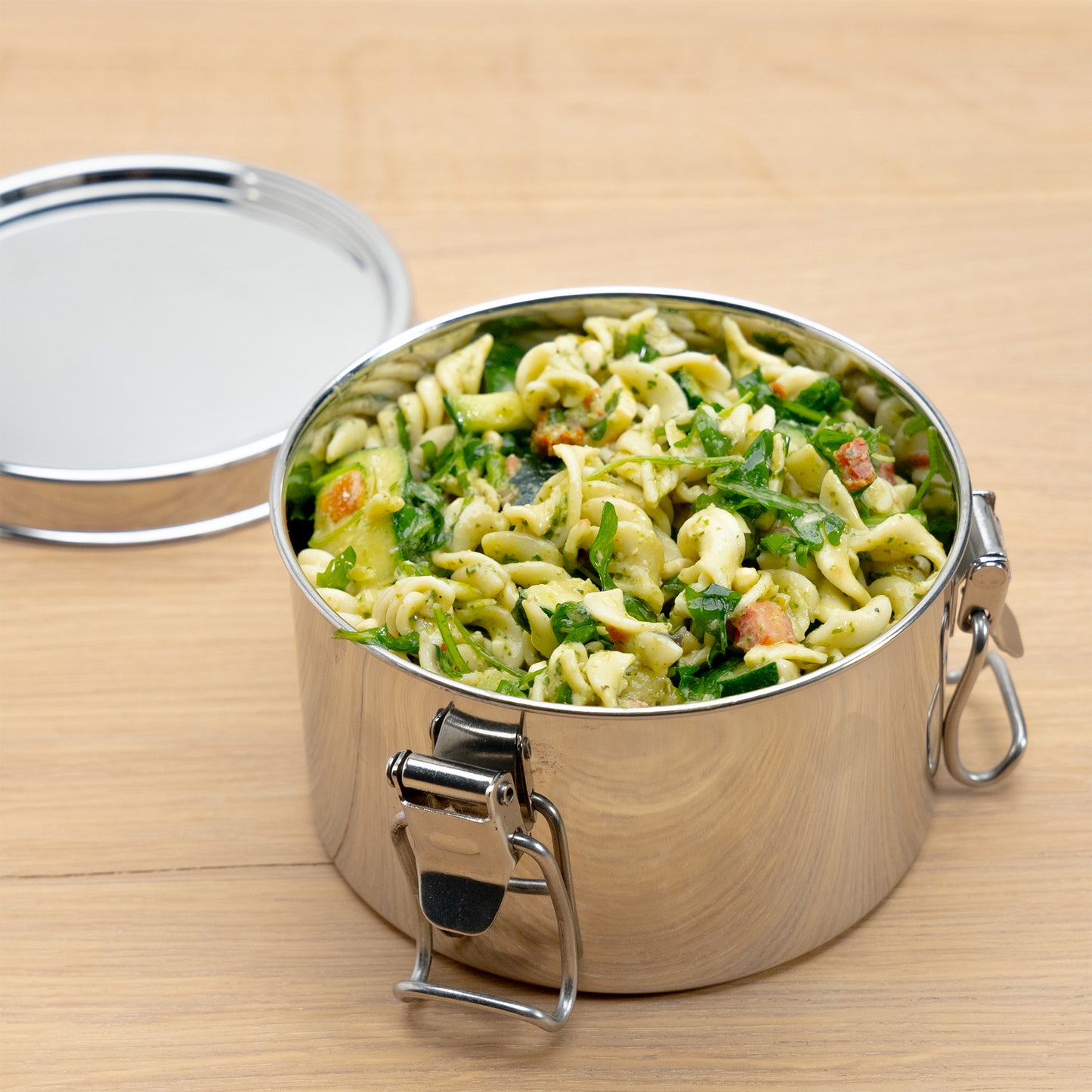 RVS lunchbox gevuld met pasta op een houten tafel