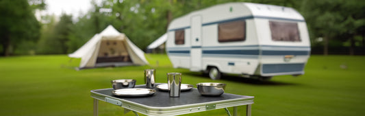 2 RVS borden en 2 bekers en 2 schalen op een tafel op een camping met een caravan en tent