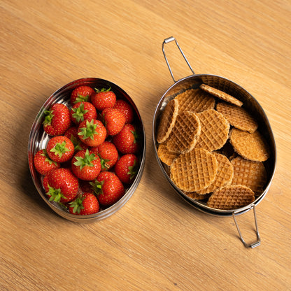 RVS lunchbox voor volwassenen met vakjes. Bovenaanzicht gevuld met aardbeien en koekjes