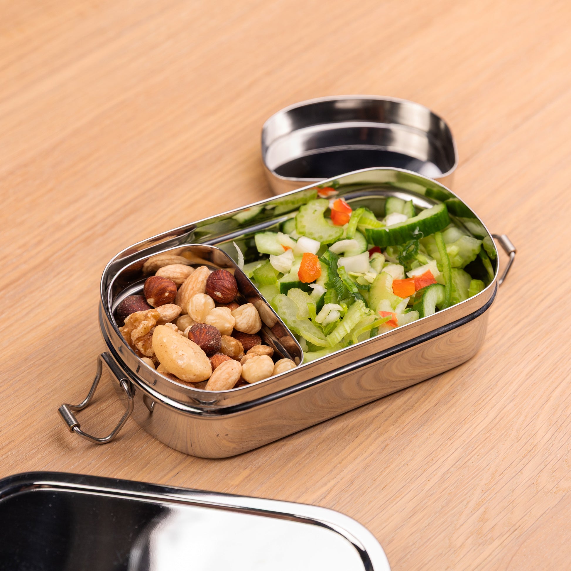 RVS lunchbox voor kinderen gevuld met noten en een salade op een school tafel